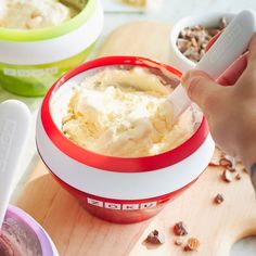 a person scooping ice cream out of a red and white bowl on top of a wooden cutting board