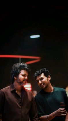 two young men standing next to each other in front of a red light at night