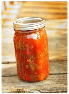 a glass jar filled with lots of red sauce on top of a wooden table next to a