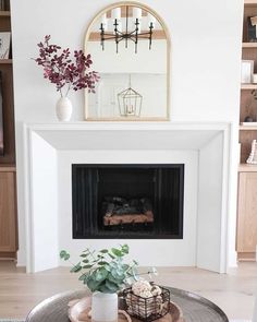 By placing a mirror on top of your fireplace mantel, the views of your room don't end at the fireplace wall. This look is infused with modern design to create an immaculate appearance, with a white mantel framing a built-in fireplace. Purple flowers add a pop of color to the white background wall...   Image: ourarkansashouse Coastal Fireplace Ideas, Coastal Fireplace, Fireplace Indoor, Fireplace White, White Mantel, Barn Door Designs, Arched Mirror, Fireplace Ideas, Fireplace Wall