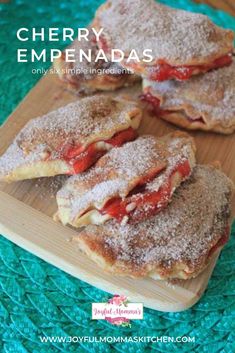 four pastries on a wooden cutting board with powdered sugar and strawberry fillings