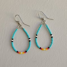 two pairs of blue and yellow beaded earrings on a white surface with silver hooks