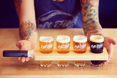 a man holding a tray with five beers on it and four glasses in front of him