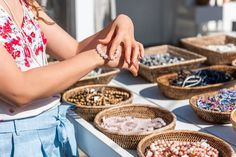 a woman standing in front of baskets filled with beads and other items on a table