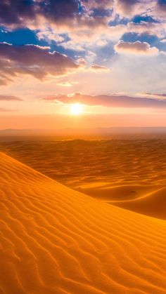 the sun is setting over sand dunes in the middle of the desert with blue sky and clouds