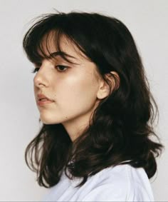 a woman with long dark hair wearing a white t - shirt looking off to the side