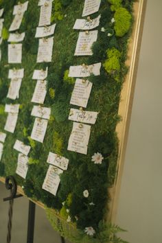 a moss covered wall with notes pinned to it and flowers on the bottom right side