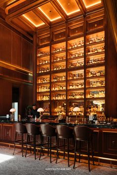 the bar is full of liquor bottles and glasses on it's shelves, along with brown leather chairs