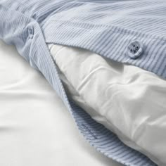 an unmade bed with white sheets and blue pinstripe comforter on it