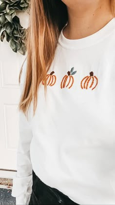 a woman wearing a white shirt with pumpkins embroidered on the front and back, standing in front of a door