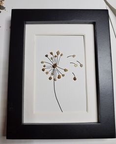 a dandelion in a black frame hanging on the wall next to a white wall