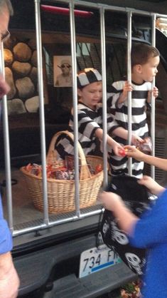 two boys in jail cell with their hands on the back of a car and one boy is holding a bag