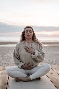 a woman is sitting on the dock with her hands in her chest and holding her stomach