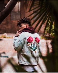 a man wearing a jacket with flowers painted on it, standing next to a palm tree