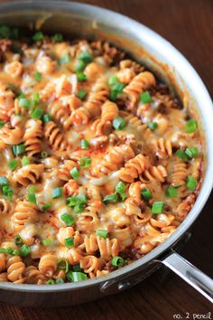 a skillet filled with macaroni and cheese on top of a wooden table