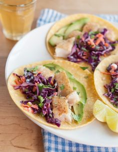 fish tacos with cole slaw and lime wedges on a plate next to a glass of water