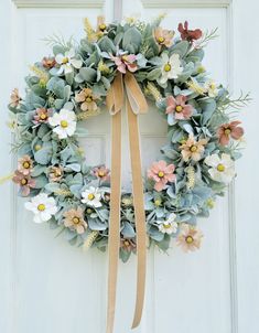 a wreath is hanging on the front door with a ribbon around it and some flowers