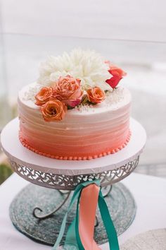 a three tiered cake with flowers on top and ribbons around the edges is sitting on a silver platter