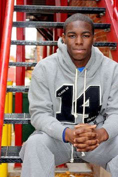 a young man sitting on top of a set of stairs wearing a sweatshirt and sweatpants