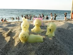 three yellow plastic figures sitting in the sand at the beach with people swimming in the water behind them