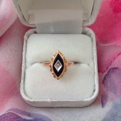 a diamond ring in a box on a pink and purple cloth covered table with flowers