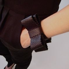 a woman's arm wearing a black top and brown leather wristband with ruffles on it