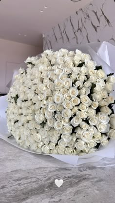 a large bouquet of white roses on a marble table with a heart shaped object in the background