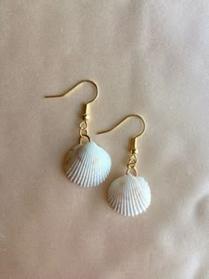 two seashells are hanging from gold earwires on a white sheet,