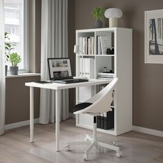 a computer desk with a laptop on top of it next to a book shelf and window