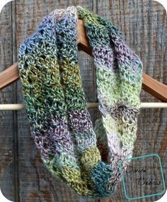 a multicolored knitted scarf hanging on a wooden hanger next to a piece of wood