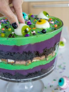 a person is decorating a cake with green and purple frosting, sprinkles and eyes