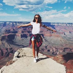 a woman standing on the edge of a cliff with her arms outstretched