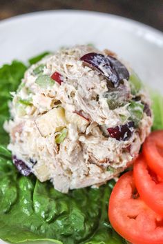 a white plate topped with lettuce, tomatoes and chicken salad on top of it