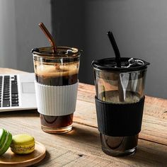 a laptop computer sitting on top of a wooden table next to a cup filled with liquid