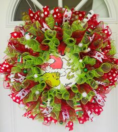 a red and green christmas wreath with santa clause on the front door hanging from a white door