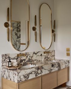 a bathroom with marble counter tops and two mirrors on the wall above it, along with gold fixtures