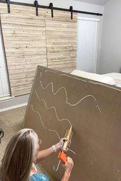 a woman is drawing on the side of a wall with an electric screwdriver