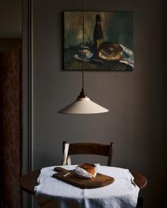 a table with a white cloth on it in front of a painting and a lamp