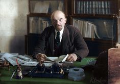 a man sitting at a desk with books and papers in front of him, holding a pair of scissors