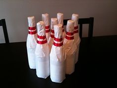 four bowling pins wrapped in white paper sitting on a black table with red ribbon around them