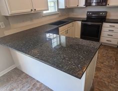 an empty kitchen with granite counter tops and white cupboards, black stove top oven and dishwasher