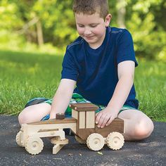 a young boy playing with a wooden toy truck on the ground in front of some grass