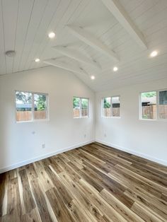 an empty room with white walls and wood flooring in the foreground, three windows on each side