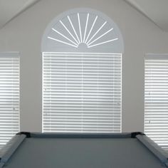 an empty pool table in front of two windows with blinds on the top and bottom