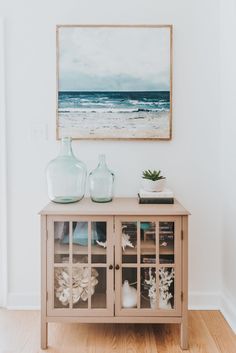 a painting hanging on the wall next to a wooden cabinet with glass doors and vases