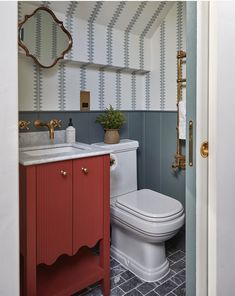 a white toilet sitting next to a red sink in a bathroom under a mirror on top of a wooden cabinet