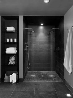 a black and white photo of a bathroom with towels on the rack, shower head, and shelves