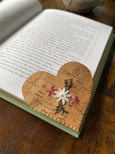 an open book on a wooden table with flowers in the shape of hearts and leaves