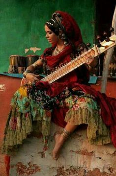 a woman sitting on top of a wall with a guitar in her hand and wearing a red dress