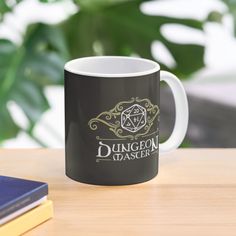 a coffee mug sitting on top of a wooden table next to a book and plant